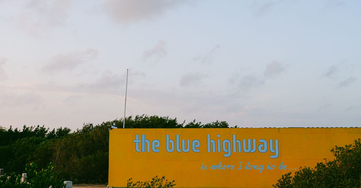 Yellow billboard with 'the blue highway' text against serene outdoor backdrop.